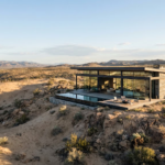 An expansive view of a serene, arid landscape with a solitary, modern glass and steel structure blending into the desert environment. Earthy color palette, wide angle, conveying isolation and high-end design.