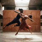 Two African contemporary dancers suspended in mid-movement inside a brutalist concrete gallery in Dakar